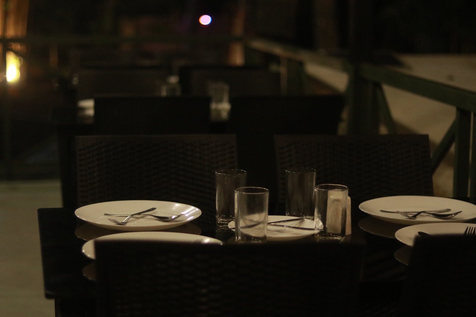 Spacious modern hotel room at JKR Gardens featuring a king-size bed with crisp white linens and a teal runner, wooden furniture, and floor-to-ceiling curtains allowing natural daylight. The room includes a tiled floor, yellow accent wall, air conditioning, and a window overlooking lush green trees, creating a peaceful and inviting atmosphere ideal for relaxation. No visible text.