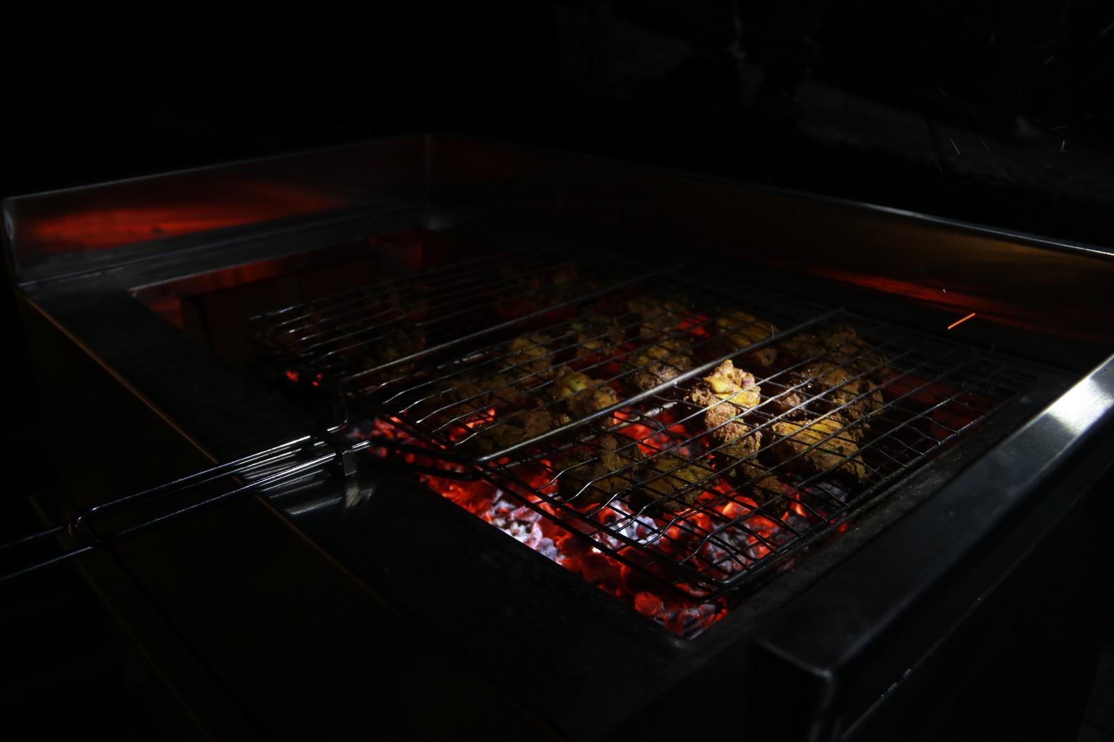 Spacious modern hotel room at JKR Gardens featuring a king-size bed with crisp white linens and a teal runner, wooden furniture, and floor-to-ceiling curtains allowing natural daylight. The room includes a tiled floor, yellow accent wall, air conditioning, and a window overlooking lush green trees, creating a peaceful and inviting atmosphere ideal for relaxation. No visible text.