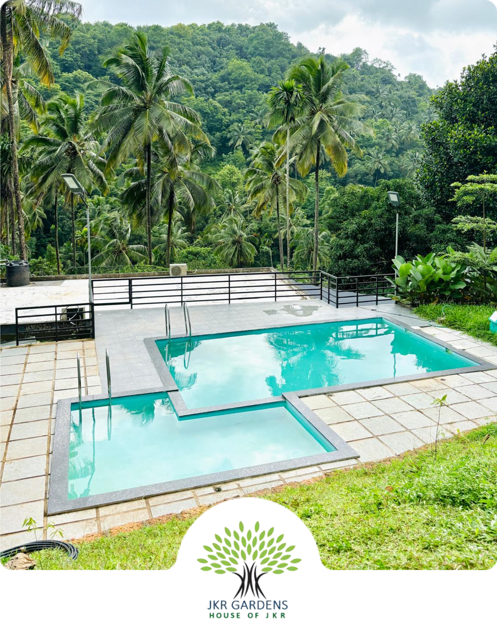 Aerial view of JKR Gardens resort surrounded by lush greenery, modern villas, and a tranquil pool area, conveying luxury and relaxation in a natural setting. No visible text.