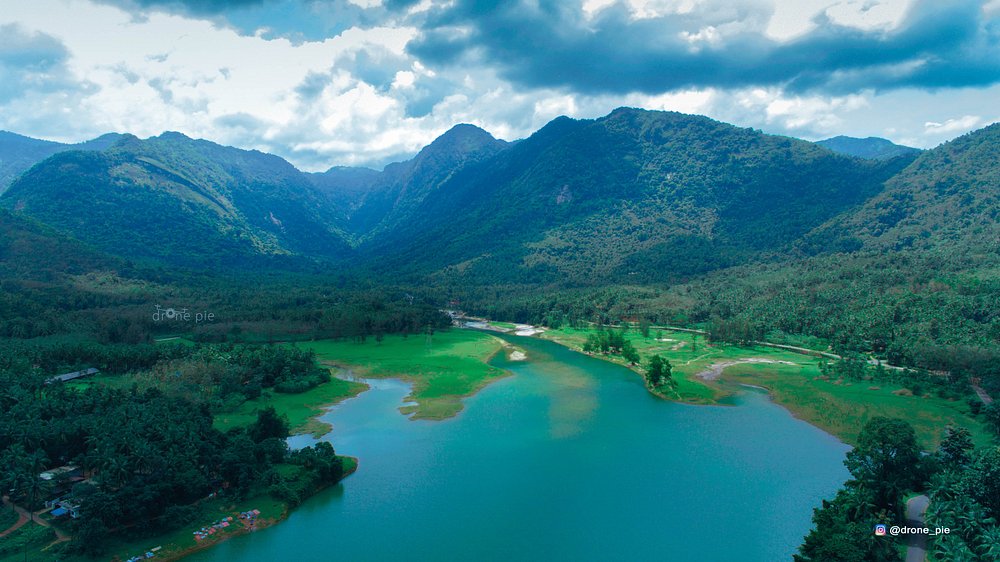 Lounge area with curved blue and orange seating and bean bags facing a large projection screen showing a Crash Bandicoot video game menu. Pink accent lighting streams from tall windows, creating a vibrant, playful environment ideal for socializing or gaming. No visible text. The mood is energetic and inviting.